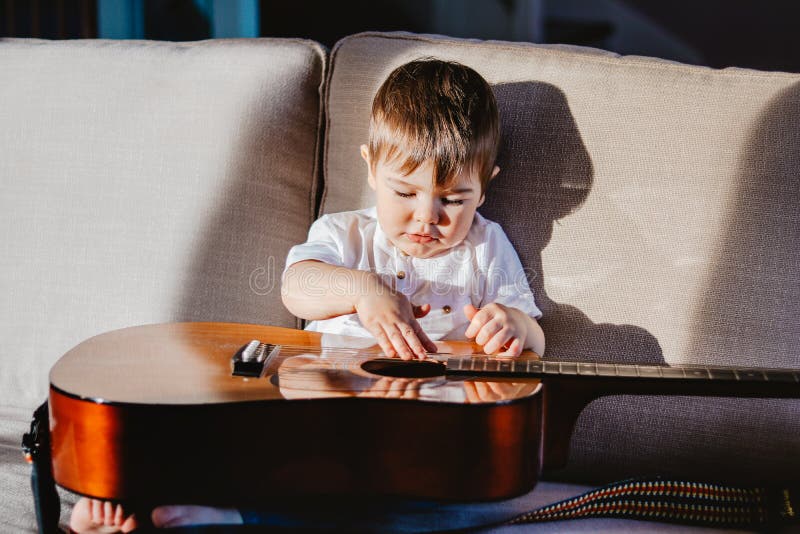Hard light portrait of cute little baby boy playing big guitar sitting on sofa. royalty free stock images Hard light portrait of cute little baby boy playing big guitar sitting on sofa. royalty free stock images