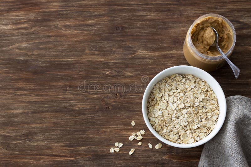 Harina de avena cruda en un cuenco blanco con la mantequilla de cacahuete, ingredientes para un desayuno sano delicioso en un fon imagen de archivo libre de regalías Harina de avena cruda en un cuenco blanco con la mantequilla de cacahuete, ingredientes para un desayuno sano delicioso en un fon imagen de archivo libre de regalías