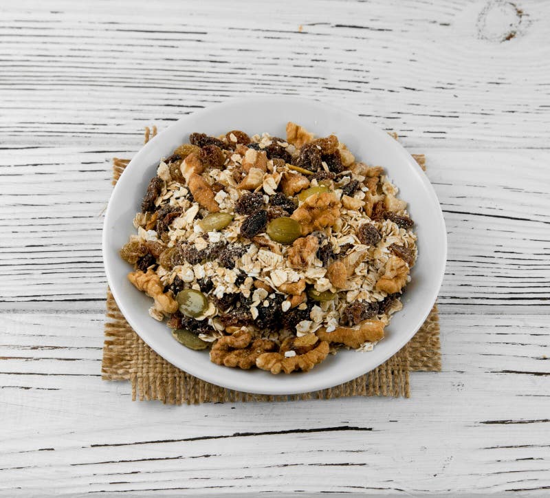 Harina de avena en cuenco con la fruta, nueces, pasas en una tabla blanca imagen de archivo libre de regalías Harina de avena en cuenco con la fruta, nueces, pasas en una tabla blanca imagen de archivo libre de regalías
