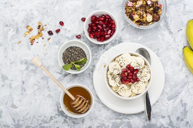 Harina de avena sana del desayuno con la granada, los plátanos, las semillas y las nueces, escena de arriba en el mármol blanco V foto de archivo Harina de avena sana del desayuno con la granada, los plátanos, las semillas y las nueces, escena de arriba en el mármol blanco V foto de archivo