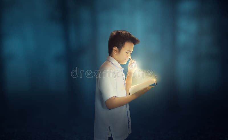 A young boy wearing school uniform reading a book in the dark forest while holding a flashlight. A young boy wearing school uniform reading a book in the dark forest while holding a flashlight.