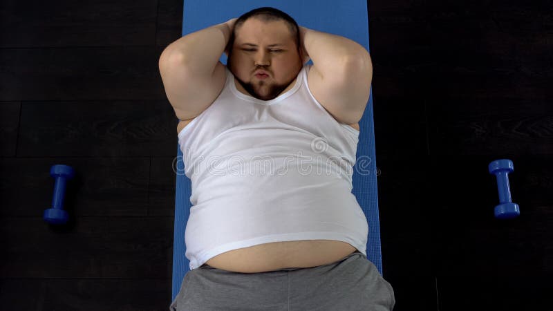 Persistent overweight man doing sit-ups lying on floor, genetic predisposition, stock photo. Persistent overweight man doing sit-ups lying on floor, genetic predisposition, stock photo