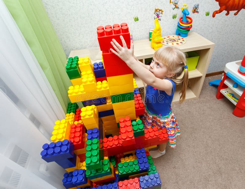 Persistent little girl building big block tower in daycare indoors. Persistent little girl building big block tower in daycare indoors