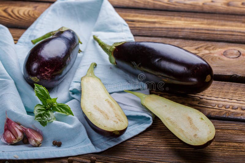 Harvest - ripe juicy eggplant. Eggplants blue towel with leaves of basil, garlic. The cut aubergine lies on a wooden kitchen table royalty free stock images Harvest - ripe juicy eggplant. Eggplants blue towel with leaves of basil, garlic. The cut aubergine lies on a wooden kitchen table royalty free stock images