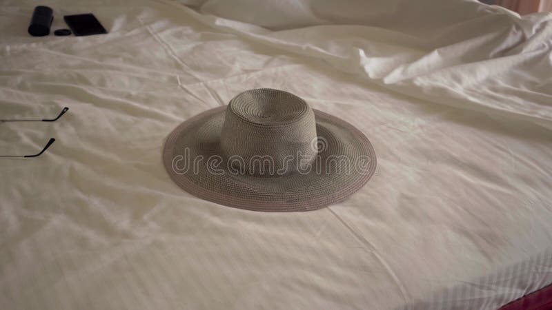 The hat lying on the bed in hotel room. Unrecognizable woman sleeping in the background in a comfortable bed. Tourism