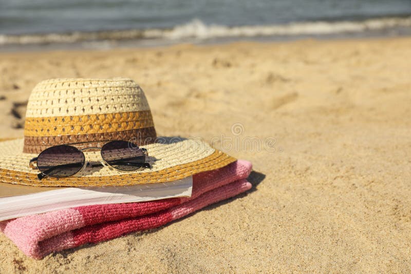 Stylish striped bag with visor cap, sunglasses and blanket on sandy beach  near sea Stock Photo