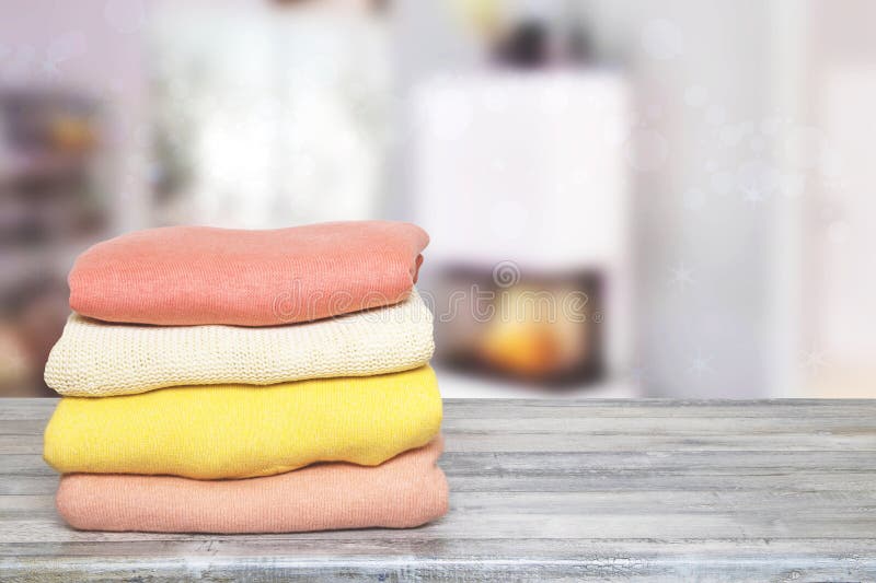 Haufen aus farbenfrohen gestrickten gemütlichen Kaschmirpullover-Pultern auf Holztisch gegen abstrakte verschwommene Wohnzimmerunt stockfotografie