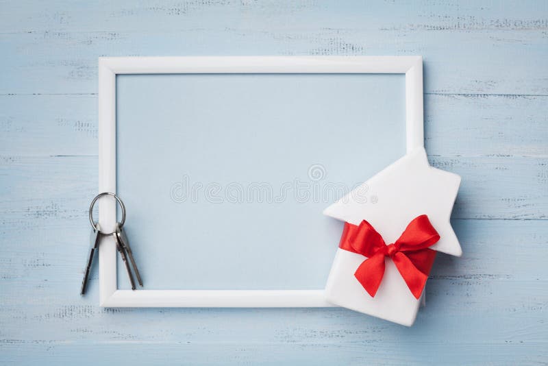 Miniature white house decorated red bow ribbon, frame and keychain on blue wooden background. Buying a new home, planning housewarming, gift or sale of real estate concept. Miniature white house decorated red bow ribbon, frame and keychain on blue wooden background. Buying a new home, planning housewarming, gift or sale of real estate concept.