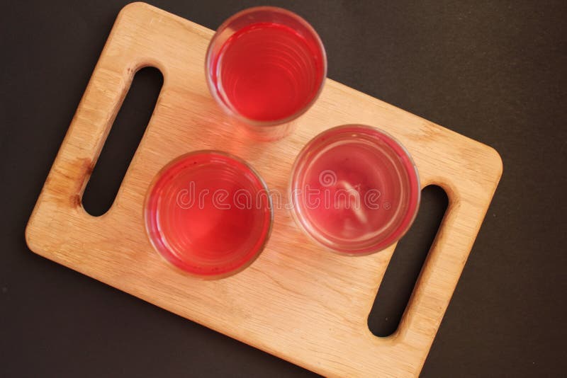 Homemade mors juice compote red pink from alina strawberry blueberries in glasses stand on a board tray on a black background. Homemade mors juice compote red pink from alina strawberry blueberries in glasses stand on a board tray on a black background.