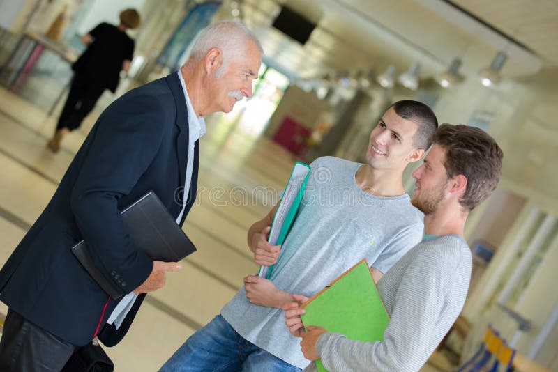 Haut maître d'école parlant aux étudiants dans le couloir photos stock Haut maître d'école parlant aux étudiants dans le couloir photos stock