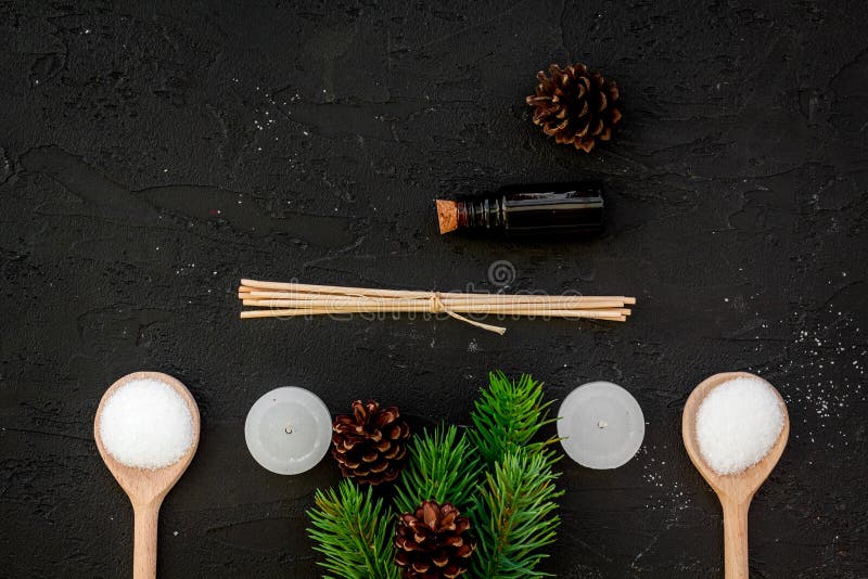 Skin care and relax. Cosmetics and aromatherapy concept. Pine spa salt, oil, spruce branch and pinecones on black background top view. Skin care and relax. Cosmetics and aromatherapy concept. Pine spa salt, oil, spruce branch and pinecones on black background top view.