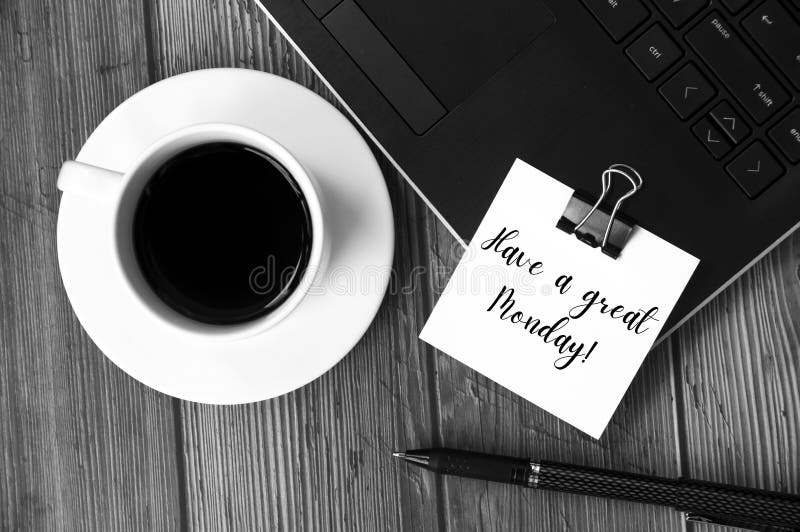 Have a great Monday text on white notepad with laptop, coffee cup and pen in black and white background. Greetings concept