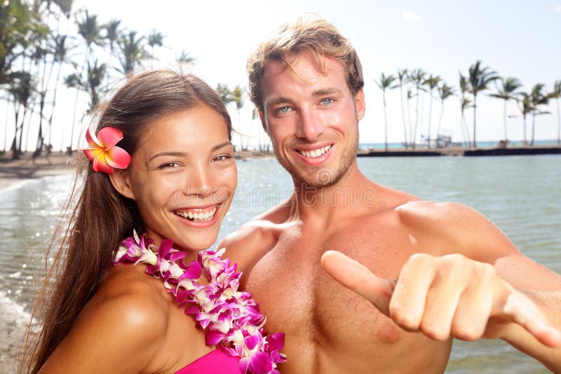 Hawaii couple happy on Hawaiian beach. Woman wearing flower lei garland and men giving shaka aloha hand sign on vacation travel. Portrait of multiracial couple ,asian mixed race woman, caucasian man. Hawaii couple happy on Hawaiian beach. Woman wearing flower lei garland and men giving shaka aloha hand sign on vacation travel. Portrait of multiracial couple ,asian mixed race woman, caucasian man