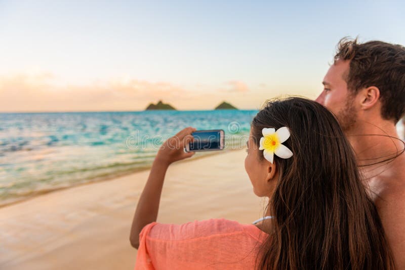 Hawaii vacation tourists taking photo with phone on romantic walk at sunset on Lanikai beach, Oahu, Hawaii honeymoon getaway. royalty free stock image Hawaii vacation tourists taking photo with phone on romantic walk at sunset on Lanikai beach, Oahu, Hawaii honeymoon getaway. royalty free stock image