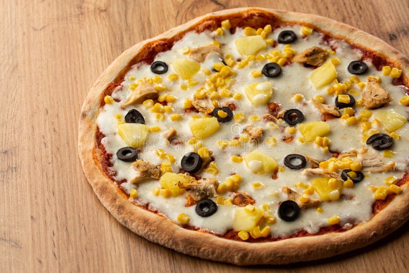 Pizza topped with sauce, chicken, cheese and pineapple serve on wooden plate on wooden table. Photo of Hawaiian pizza. royalty free stock photography Pizza topped with sauce, chicken, cheese and pineapple serve on wooden plate on wooden table. Photo of Hawaiian pizza. royalty free stock photography
