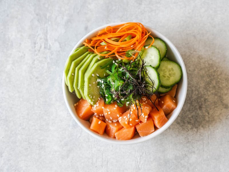 Hawaiian salmon poke bowl with rice, avocado, cucumber, carrot, chukka and sesame seeds on a gray background. top view