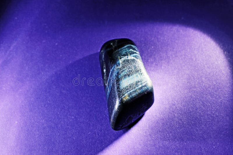 Hawkeye gemstone close up illuminated on a purple background.