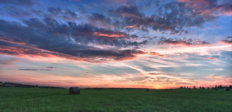 Hay bales on a meadow against beautiful sky with clouds in sunset