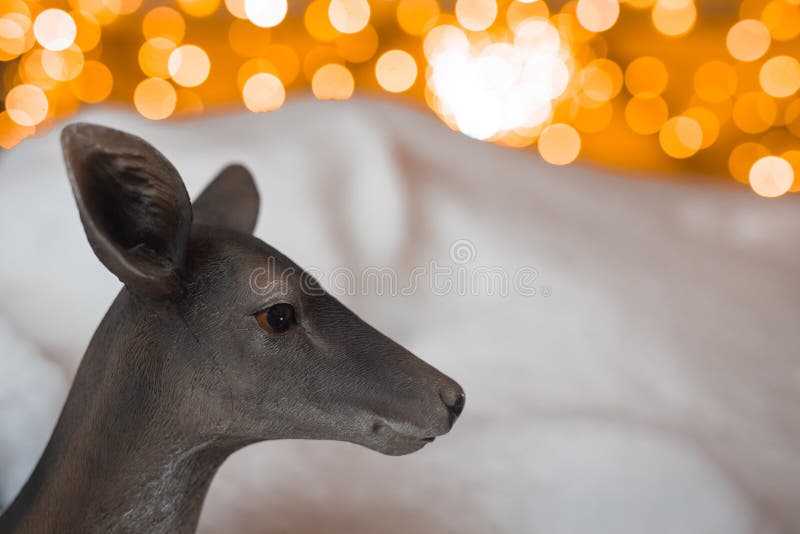 Head of a plastic deer posing in front of a white snow and some christmas decor lighting