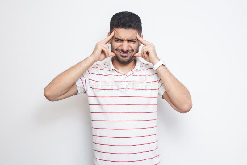 Headache or confution. Portrait of confused handsome bearded young man in striped t-shirt standing, holding his painful head or stock images Headache or confution. Portrait of confused handsome bearded young man in striped t-shirt standing, holding his painful head or stock images