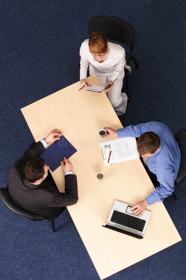 Businesspeople gathered around a table for a meeting, interview. Aerial shot taken from directly above the table. Businesspeople gathered around a table for a meeting, interview. Aerial shot taken from directly above the table.