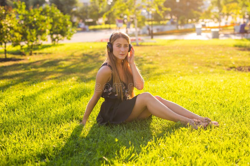 Headphones concept. Beautiful girl relaxing and listen music in the headphones in the city park on background. Woman in