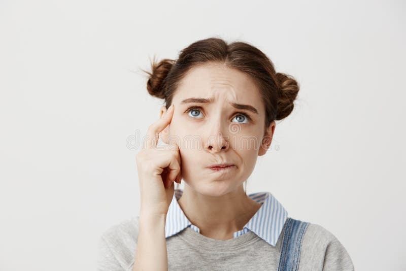 Headshot of adult girl looking up with frown expressing misunderstanding. Cute female student twisting mouth trying to stock photography Headshot of adult girl looking up with frown expressing misunderstanding. Cute female student twisting mouth trying to stock photography