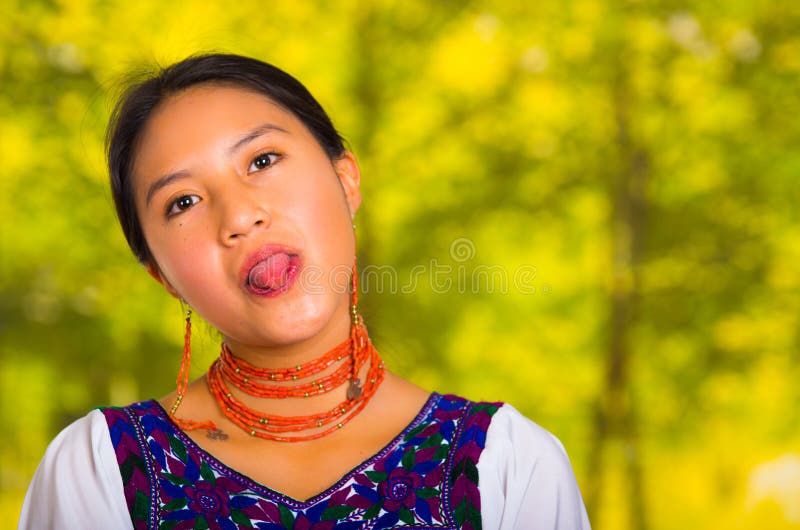 Headshot beautiful young woman wearing traditional andean blouse with red necklace, posing for camera holding tongue out stock photos Headshot beautiful young woman wearing traditional andean blouse with red necklace, posing for camera holding tongue out stock photos