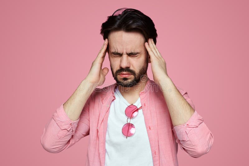 Headshot de um menino novo forçado vestido na camisa cor-de-rosa que tem uma dor de cabeça isolado sobre o fundo cor-de-rosa fotografia de stock Headshot de um menino novo forçado vestido na camisa cor-de-rosa que tem uma dor de cabeça isolado sobre o fundo cor-de-rosa fotografia de stock