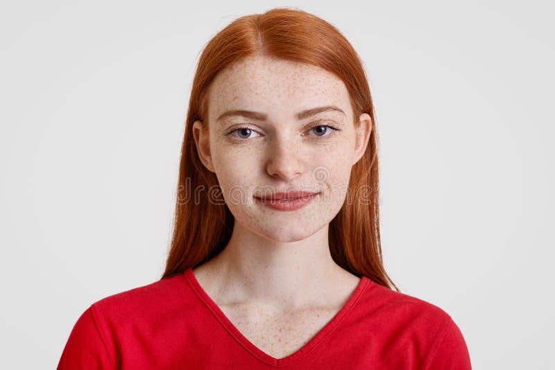 Headshot van vrij freckled roodharigewijfje bekijkt met vriendschappelijke uitdrukking camera, gekleed in rode sweater, stelt teg stock foto Headshot van vrij freckled roodharigewijfje bekijkt met vriendschappelijke uitdrukking camera, gekleed in rode sweater, stelt teg stock foto