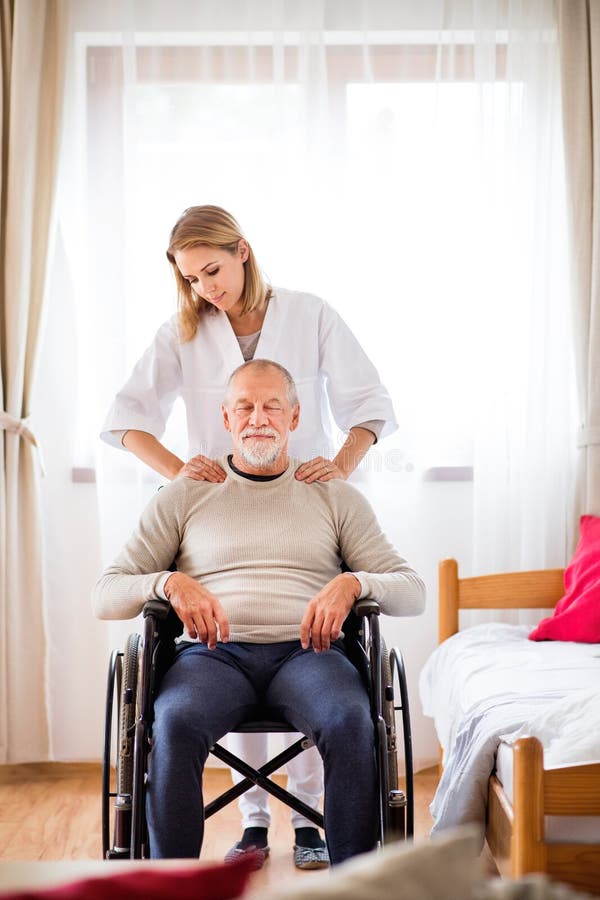 Health visitor and a senior men in a wheelchair during home visit. A nurse or a physiotherapist giving men shoulder massage. Health visitor and a senior men in a wheelchair during home visit. A nurse or a physiotherapist giving men shoulder massage.