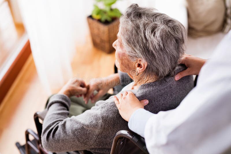 Health visitor and a senior woman during home visit. Unrecognizable nurse giving woman shoulder massage.