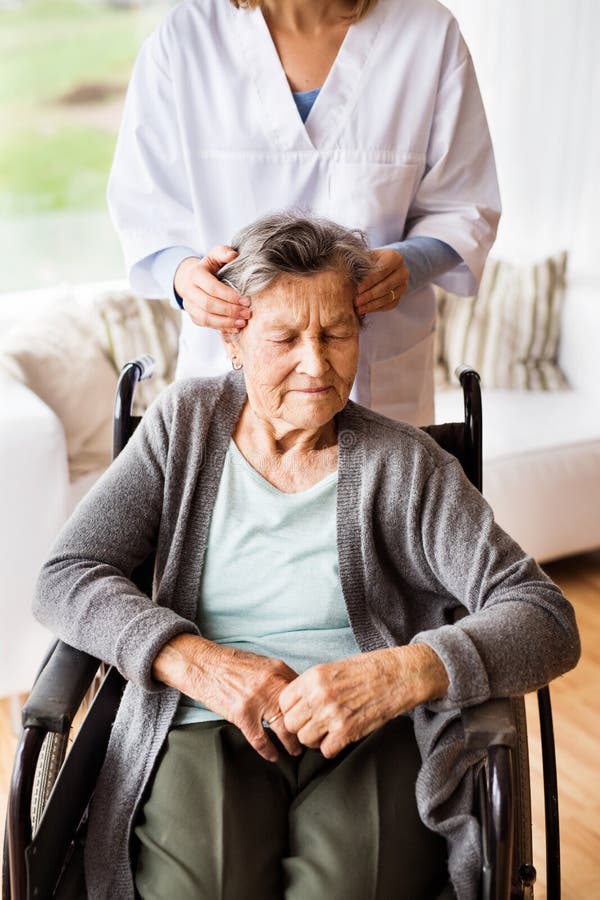 Health visitor and a senior women during home visit. Unrecognizable nurse giving women temple massage. Health visitor and a senior women during home visit. Unrecognizable nurse giving women temple massage.