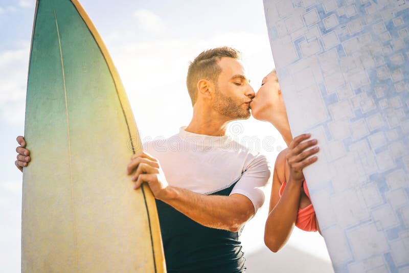 Health young couple of surfers kissing at sunset on the beach holding surfboards - Happy lovers having a tender moment with a kiss royalty free stock photos Health young couple of surfers kissing at sunset on the beach holding surfboards - Happy lovers having a tender moment with a kiss royalty free stock photos