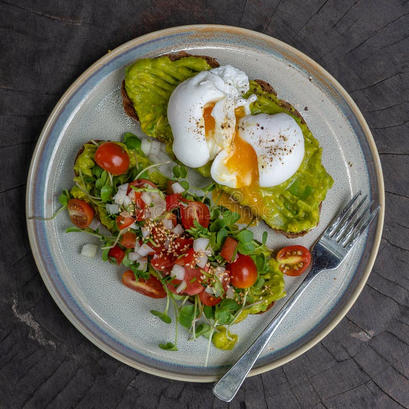 Healthy breakfast with bread toast and poached egg with green salad, red tomato and smashed avocado