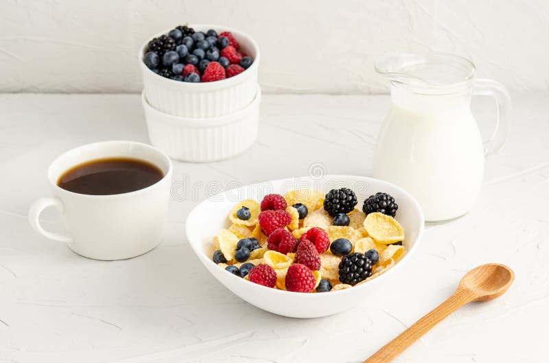 Healthy breakfast with cornflakes in a white plate, berries, milk and coffee on a white background