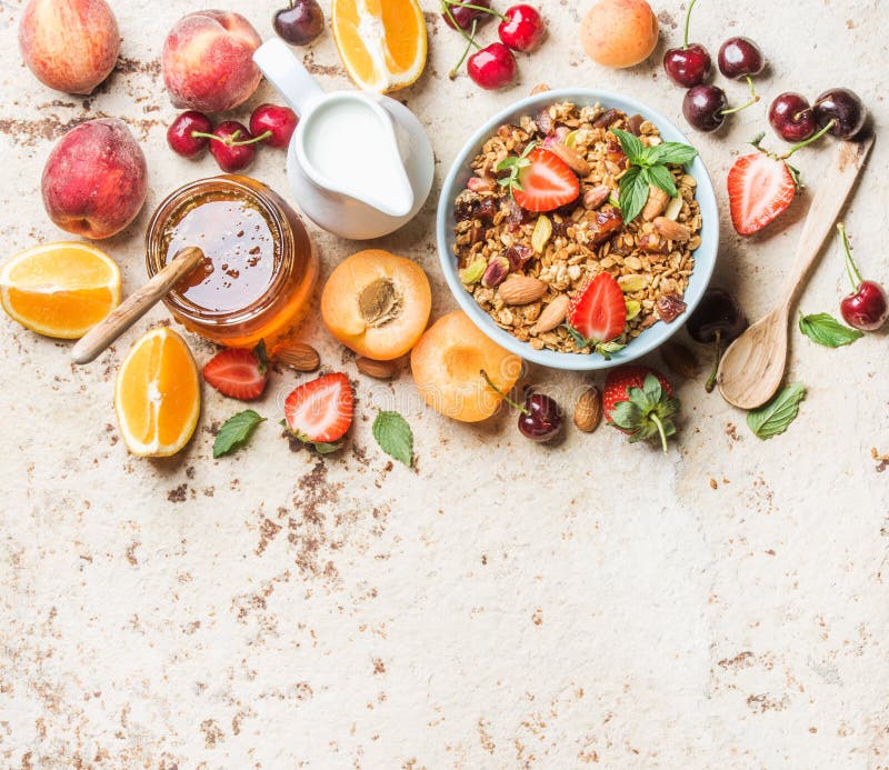 Healthy breakfast ingredients. Oat granola in bowl with nuts, strawberry and mint, milk in jug, honey in glass jar