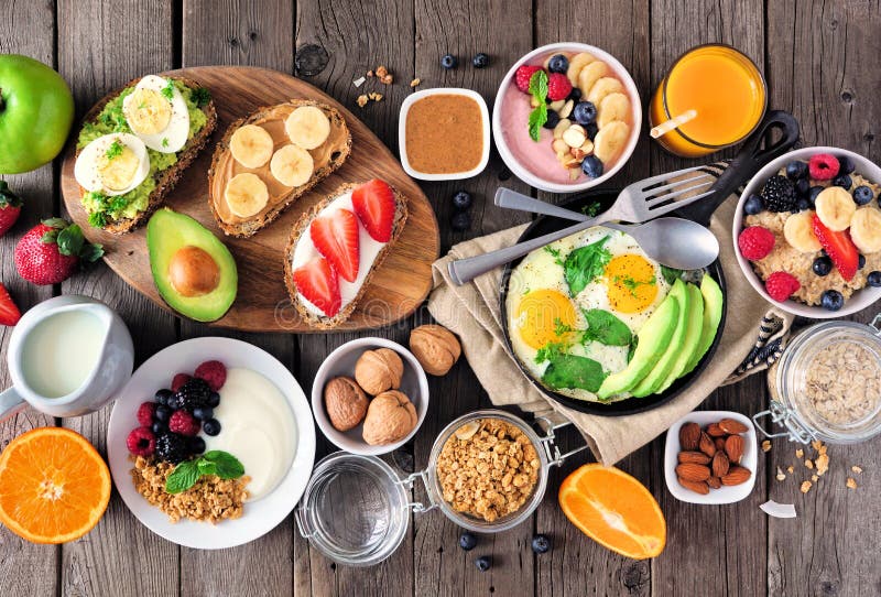 Healthy breakfast table scene with fruit, yogurts, oatmeal, smoothie, nutritious toasts and egg skillet, top view over wood royalty free stock photo