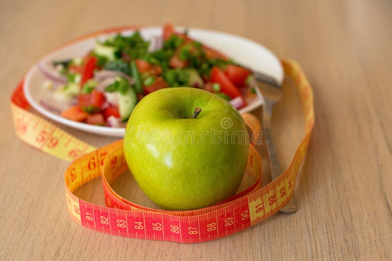 Healthy eating, dieting, slimming and weigh loss concept - close up of green apple, measuring tape and salad.