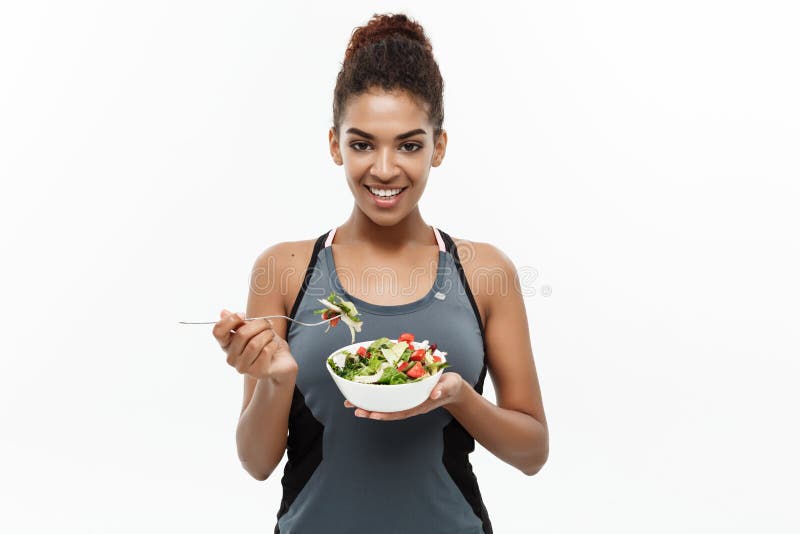 Healthy and Fitness concept - Beautiful American African lady in fitness clothes on diet eating fresh salad. Isolated on. White background royalty free stock images Healthy and Fitness concept - Beautiful American African lady in fitness clothes on diet eating fresh salad. Isolated on. White background royalty free stock images