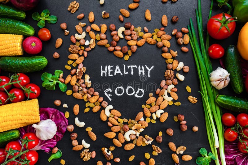 Healthy food background. Healthy food concept with fresh vegetables for cooking and some kind types of nuts. The phrase `Healthy food` is in the middle on the heart made from nuts. Dark background.