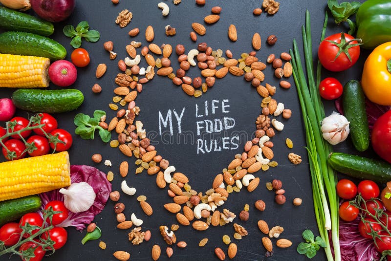 Healthy food background. Healthy food concept with fresh vegetables for cooking and some kind types of nuts. The phrase `My life, my food, my rules` is in the middle on the heart made from nuts. Dark background.