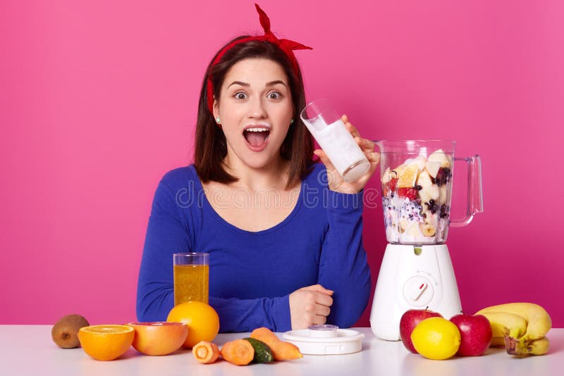 Healthy food concept. Close up of a young woman uses berries and bananas for making smoothie. Astonished lady againest pink studio royalty free stock photo Healthy food concept. Close up of a young woman uses berries and bananas for making smoothie. Astonished lady againest pink studio royalty free stock photo