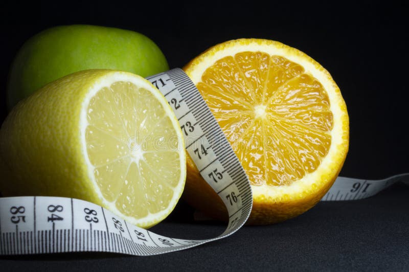 Healthy food: fresh fruit and measuring tape on black background