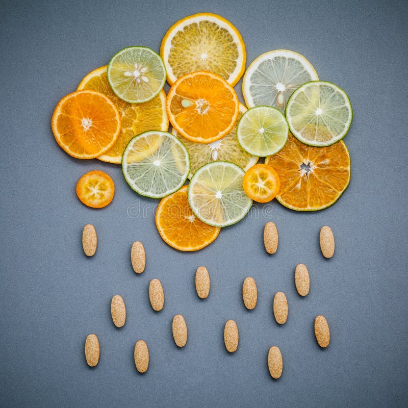 Healthy foods and medicine concept. Pills of vitamin C and citrus fruits in the shape of cloud and raining. Citrus fruits sliced lime,orange and lemon on gray background flat lay.