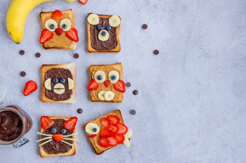 Healthy funny face sandwiches for kids. Animal faces toast with peanut and hazelnat chocolate butter, banana, strawberry and blueberry. Horizontal orientation. Copy space. Top view