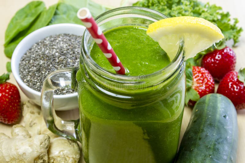 Verde sano succo frullato, circondato da tutta la frutta, verdura e semi di chia con limone per guarnire e rosso a pois di paglia.