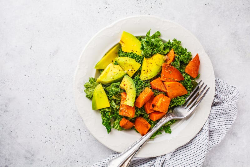 Healthy green kale salad with avocado and baked sweet potatoes, copy space. Plant based diet concept, detox food