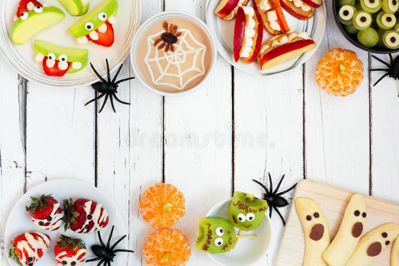 Healthy Halloween fruit snacks. Assortment of fun, spooky treats. Above view double border over a white wood background with copy space. Healthy Halloween fruit snacks. Assortment of fun, spooky treats. Above view double border over a white wood background with copy space