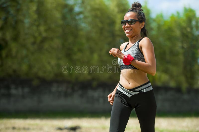 Healthy lifestyle portrait of young happy and fit Southeast Asian Thai runner woman in running workout outdoors at green field bac